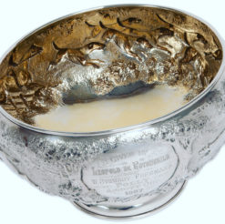 A magnificent and rare large Silver Victorian Rose Bowl with a chased fox hunting scene, depicting three and a half couple of hounds pursuing a fox in open landscape with the huntsman jumping a post and rail fence, a gentleman mounted with top hat and a house, most likely Ascott house. Makers: James Berkeley Hennel, London 1884. Includes Company Trade Mark. Weight 55 Ounces. Gilt Interior. IMPORTANT Rothschild connection. The Inscription is set between two oak trees and reads, “Given by Leopold De Rothschild, Won By W. Stewart-Freeman’s Folly, Ascott Cup 1887”